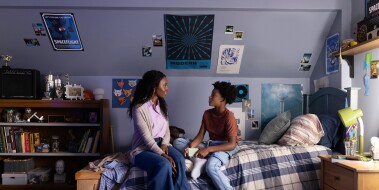 An African American mother and her son sitting on his bed looking at each other.